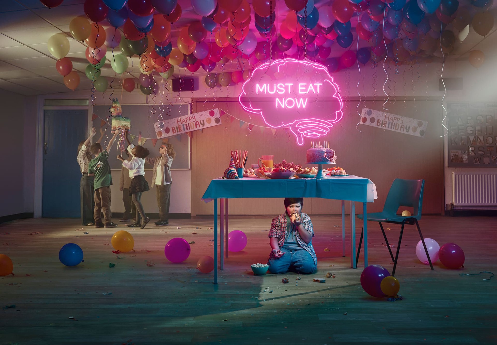 Boy sitting under a table and eating at a birthday party. Actor portrayal.